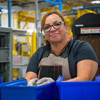 Woman with gloves putting items into blue bin.